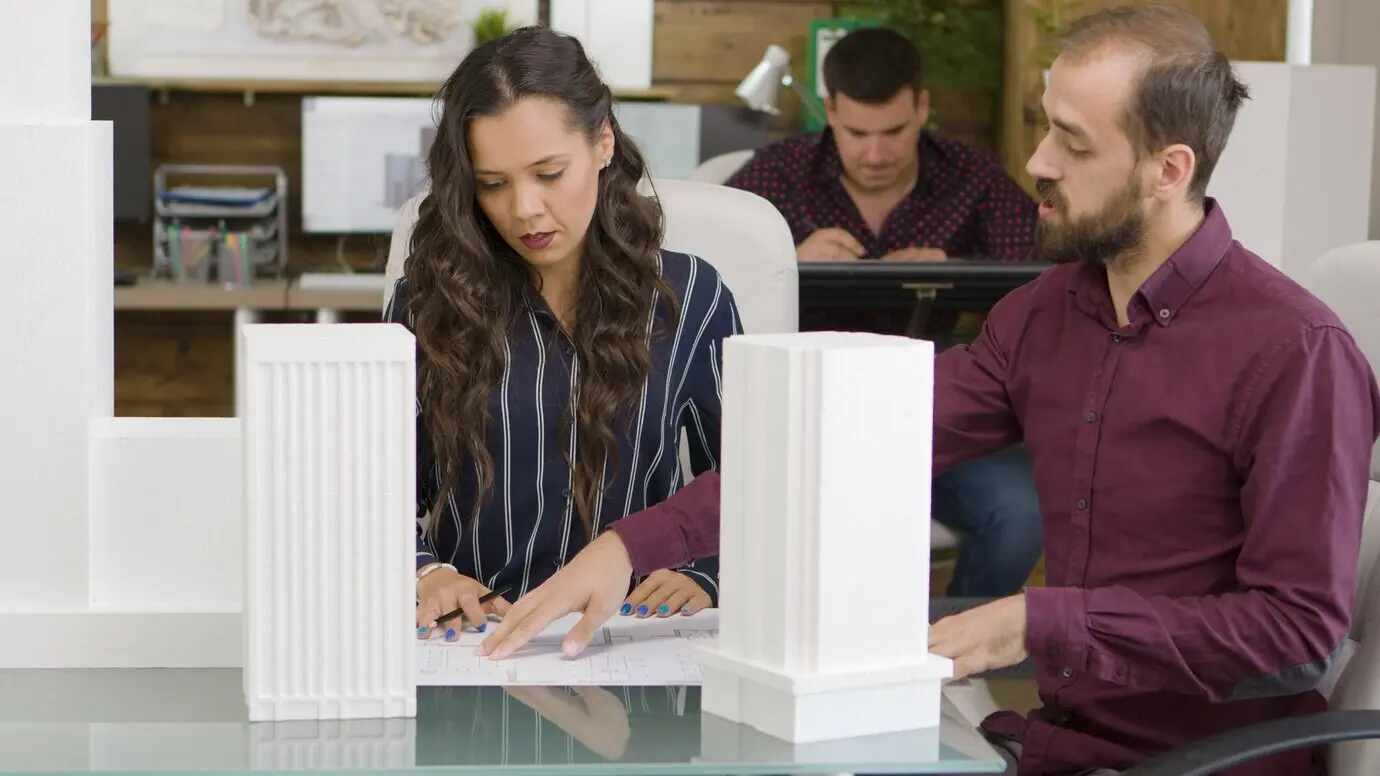 An architect and a designer collaborating on 3D-printed building models in a modern office